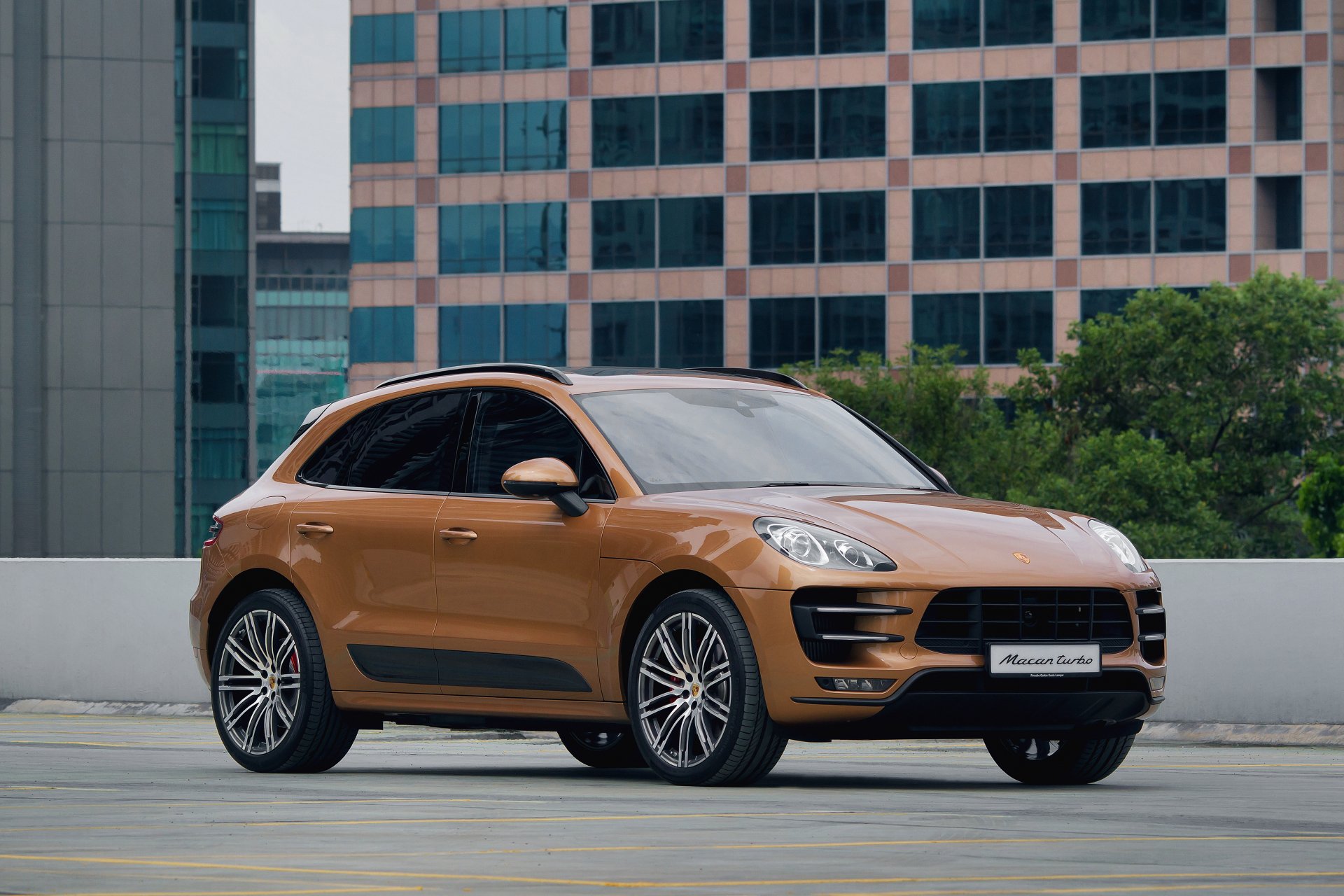 Bronze Porsche Macan SUV parked on a rooftop with city high-rises in the background — 4K Ultra HD PC desktop wallpaper/background of a Porsche vehicle.