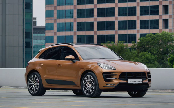 Bronze Porsche Macan SUV parked on a rooftop with city high-rises in the background — 4K Ultra HD PC desktop wallpaper/background of a Porsche vehicle.