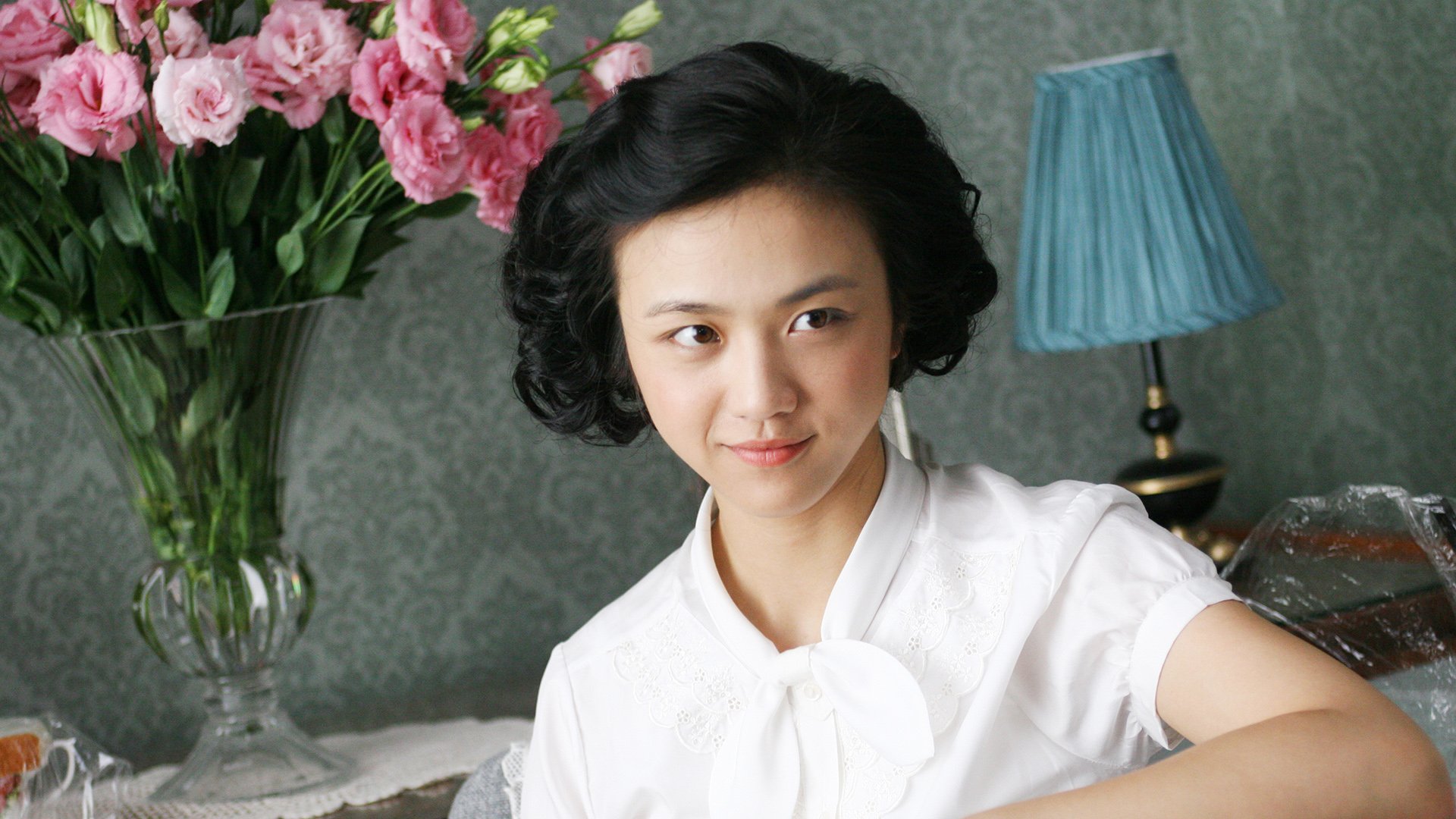 A scene from the movie Lust, Caution, featuring a woman with short black hair and a white blouse, used as an HD desktop wallpaper and background. In the background, there's a vase with pink flowers and a blue lamp.