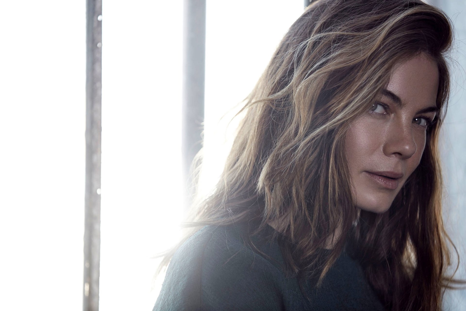 HD desktop wallpaper close-up of a brunette woman's face, long hair and soft backlight, natural makeup and a calm, contemplative expression.