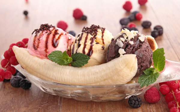 HD desktop wallpaper of a banana split featuring scoops of berry, vanilla, and chocolate ice cream, topped with chocolate syrup and surrounded by fresh berries and mint leaves.