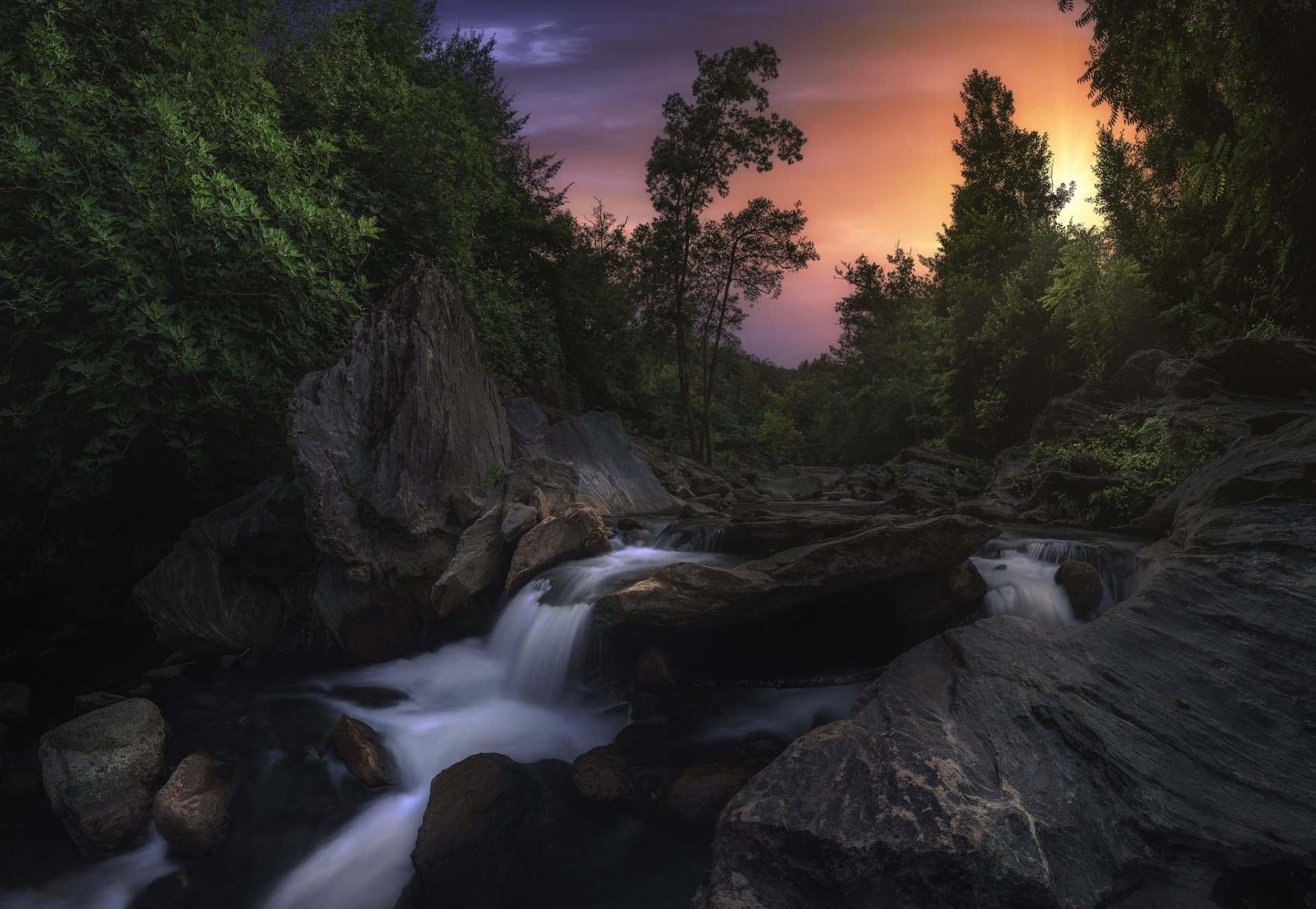 HD PC desktop wallpaper and background: a nature stream winding through a rocky forest at sunset, white foam swirling over dark stones and pooling among mossy boulders.