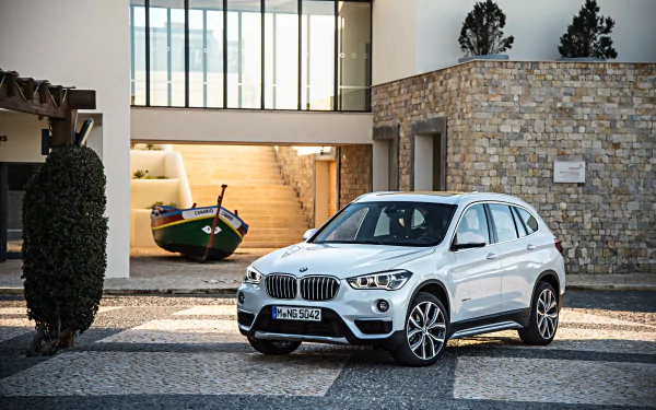 A white BMW X1 SUV parked in front of a stone building with large windows, captured in 4K Ultra HD as a PC desktop wallpaper and background.