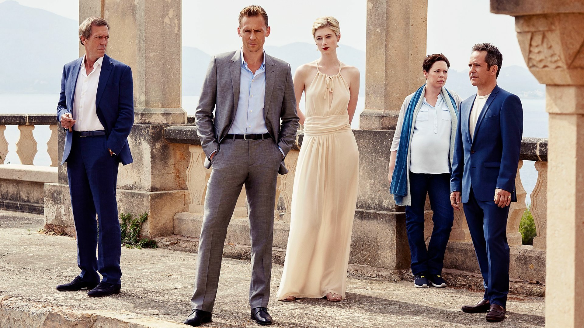 HD desktop wallpaper of five elegantly dressed figures on a sunlit stone terrace with columns, posed like a promotional image for the TV drama The Night Manager.
