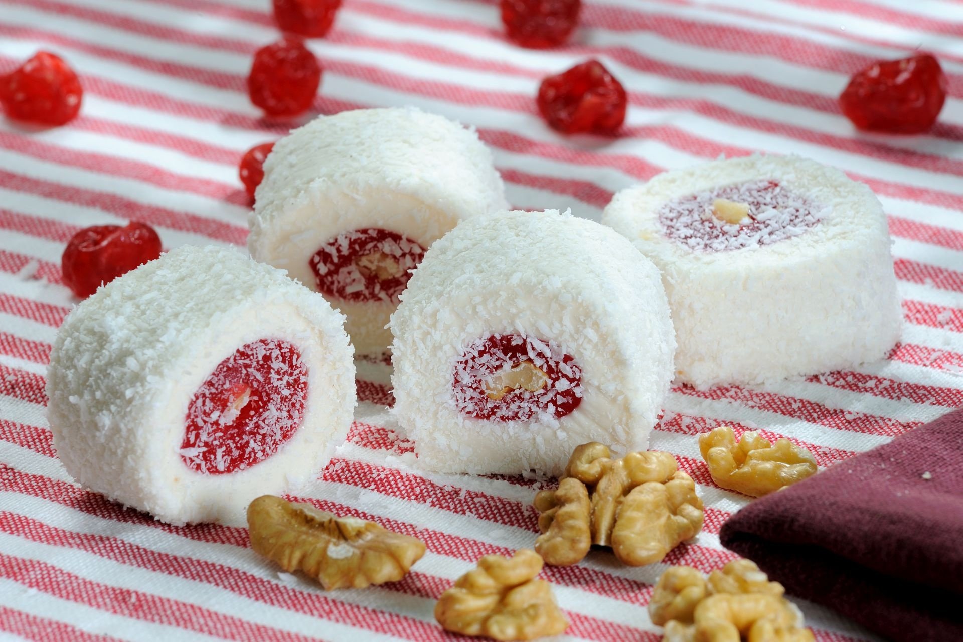 HD PC desktop wallpaper featuring white coconut-covered sweets with red filling, scattered walnuts, and red berries on a striped cloth background.