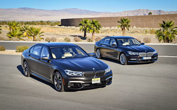 Two black BMW 7 Series vehicles parked on a desert road with palm trees and mountains in the background, captured in 4K Ultra HD desktop wallpaper quality.
