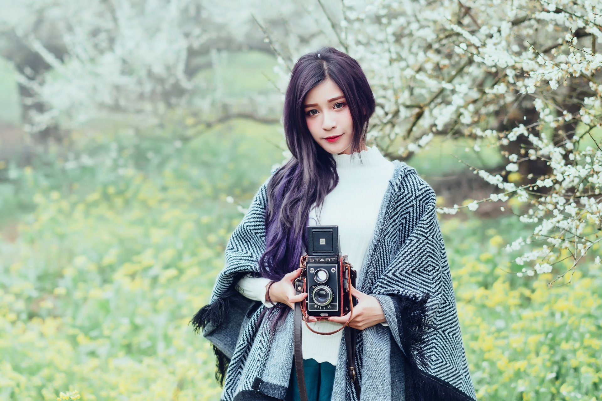 Woman model with long purple hair holding a vintage camera among spring blossoms, shallow depth of field; HD PC desktop wallpaper/background.