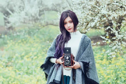 Woman model with long purple hair holding a vintage camera among spring blossoms, shallow depth of field; HD PC desktop wallpaper/background.
