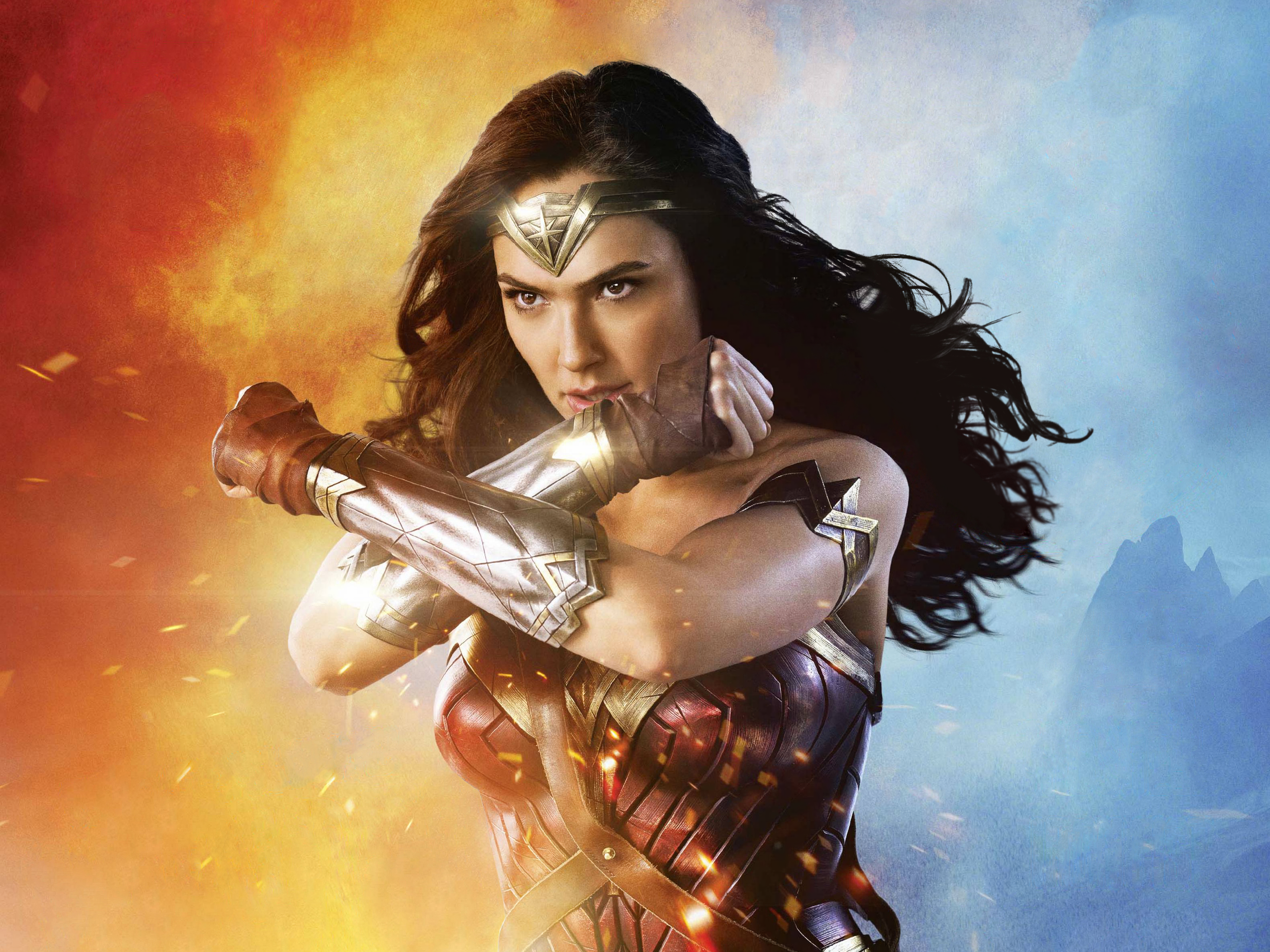 HD wallpaper featuring Gal Gadot as Wonder Woman from DC Comics, striking a powerful pose with arms crossed against a dynamic fiery and cool toned background.