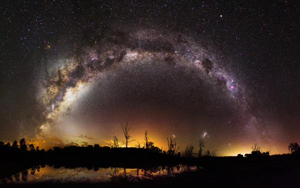 A breathtaking HD desktop wallpaper featuring the starry night sky and the Milky Way arching over a tranquil water body, with stars reflecting on the surface, creating a Sci-Fi ambiance.