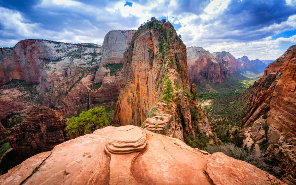 HD image of a breathtaking landscape in Zion National Park, Utah, featuring a stunning red-rock canyon valley surrounded by rugged mountains under a vivid blue sky with scattered clouds.