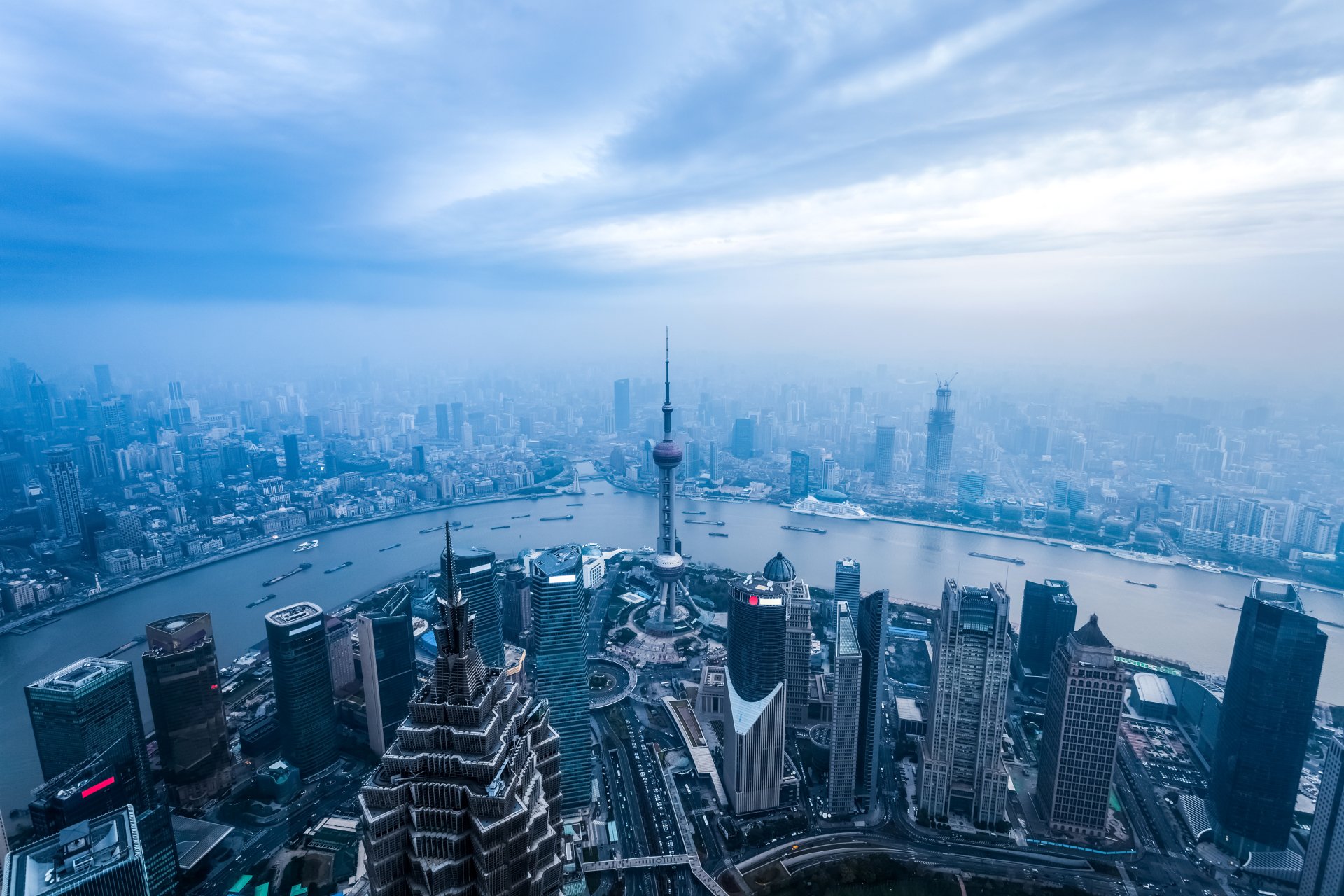 Aerial view of Shanghai cityscape featuring the Oriental Pearl Tower, skyscrapers, and the river under a cloudy sky in 4K Ultra HD.
