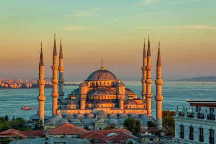 The Sultan Ahmed Mosque in Istanbul, Turkey, glows at sunset with its iconic domes and six minarets against a backdrop of the sea and cityscape.