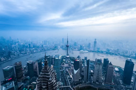 Aerial view of Shanghai cityscape featuring the Oriental Pearl Tower, skyscrapers, and the river under a cloudy sky in 4K Ultra HD.