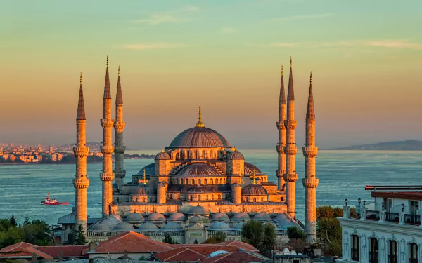 The Sultan Ahmed Mosque in Istanbul, Turkey, glows at sunset with its iconic domes and six minarets against a backdrop of the sea and cityscape.