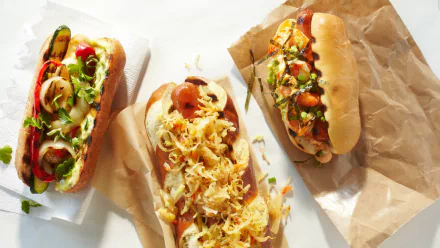 HD PC desktop wallpaper background: three gourmet hot dogs topped with pickles, peppers, shredded cabbage and sauces on parchment and white backdrop (food, hot dog)