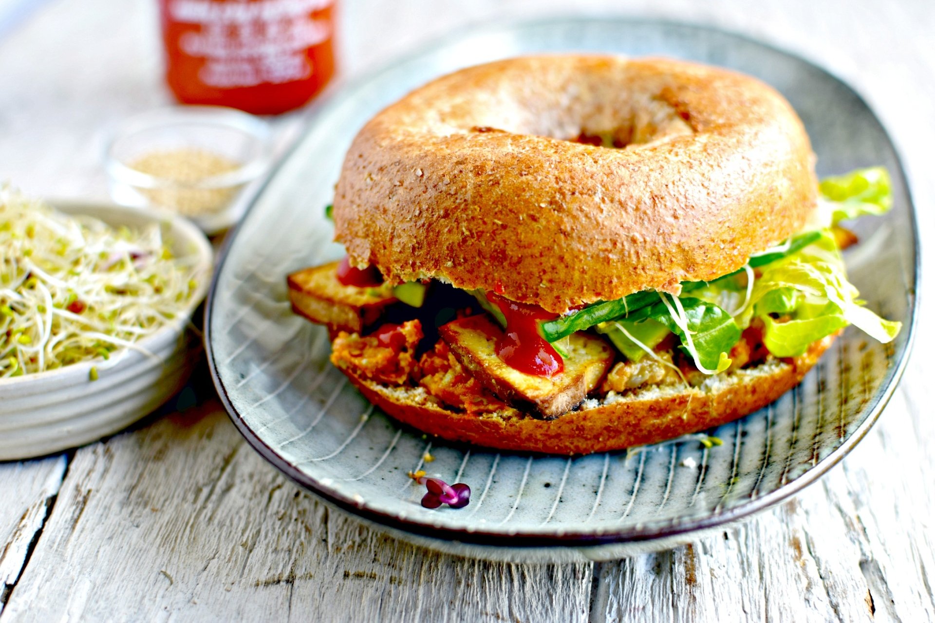 HD PC desktop wallpaper/background of food: a toasted bagel sandwich on hearty bread, filled with greens, roasted vegetables and spread on a plate, with a small bowl of sprouts beside it.