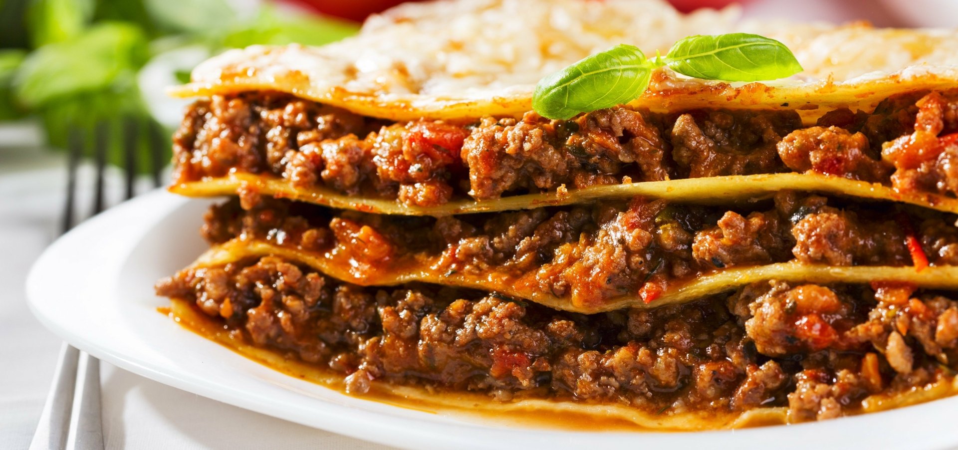 Close-up of a meaty lasagna meal with melted cheese and basil, presented as a vivid 2K Quad HD PC desktop wallpaper/background.