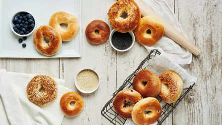5K Ultra HD PC desktop wallpaper: assorted blueberry bagels and bread on a rustic white table with bowls of blueberries and seeds, styled food background.