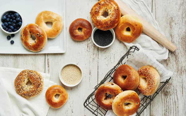 5K Ultra HD PC desktop wallpaper: assorted blueberry bagels and bread on a rustic white table with bowls of blueberries and seeds, styled food background.