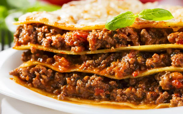 Close-up of a meaty lasagna meal with melted cheese and basil, presented as a vivid 2K Quad HD PC desktop wallpaper/background.