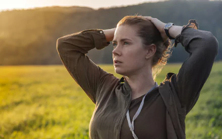 Amy Adams in a scene from the movie Arrival, captured in a 4K Ultra HD PC desktop wallpaper showing her thoughtful expression against a sunlit field background.