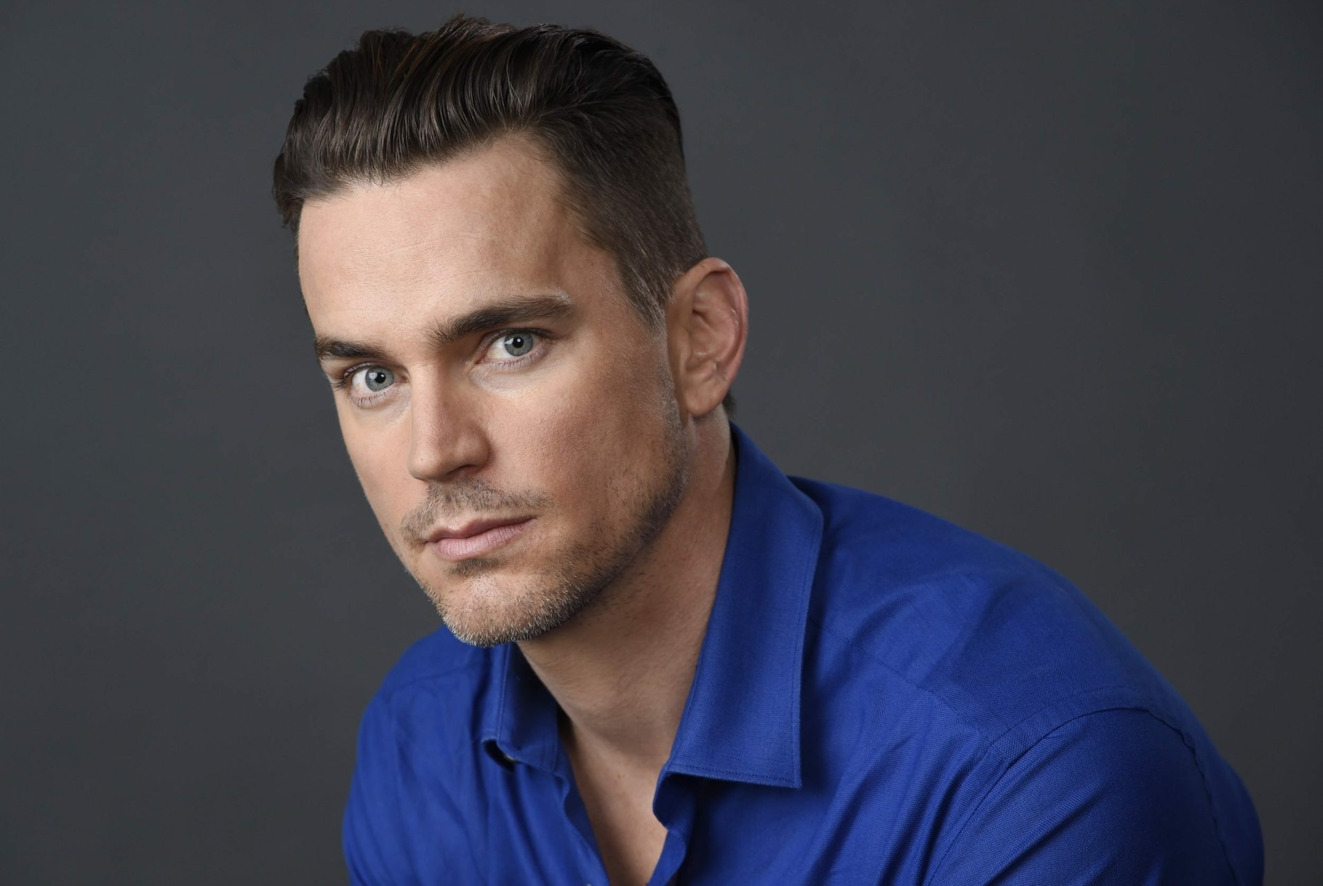 HD desktop wallpaper featuring a man in a blue shirt with an intense gaze, on a grey background.
