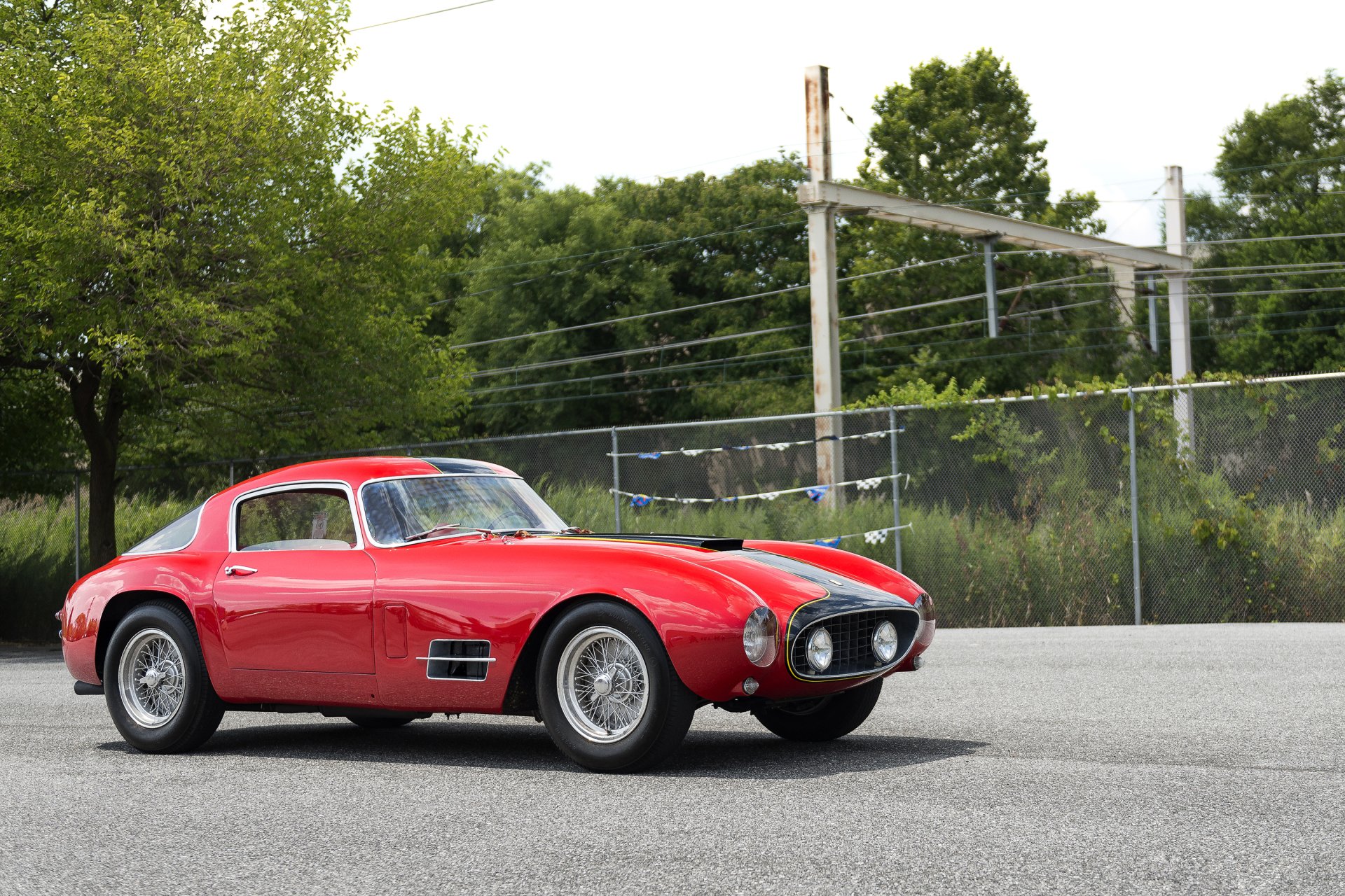 Red Ferrari 250 GT sports car parked on pavement with trees and chain‑link fence backdrop — 2K Quad HD PC desktop wallpaper background.