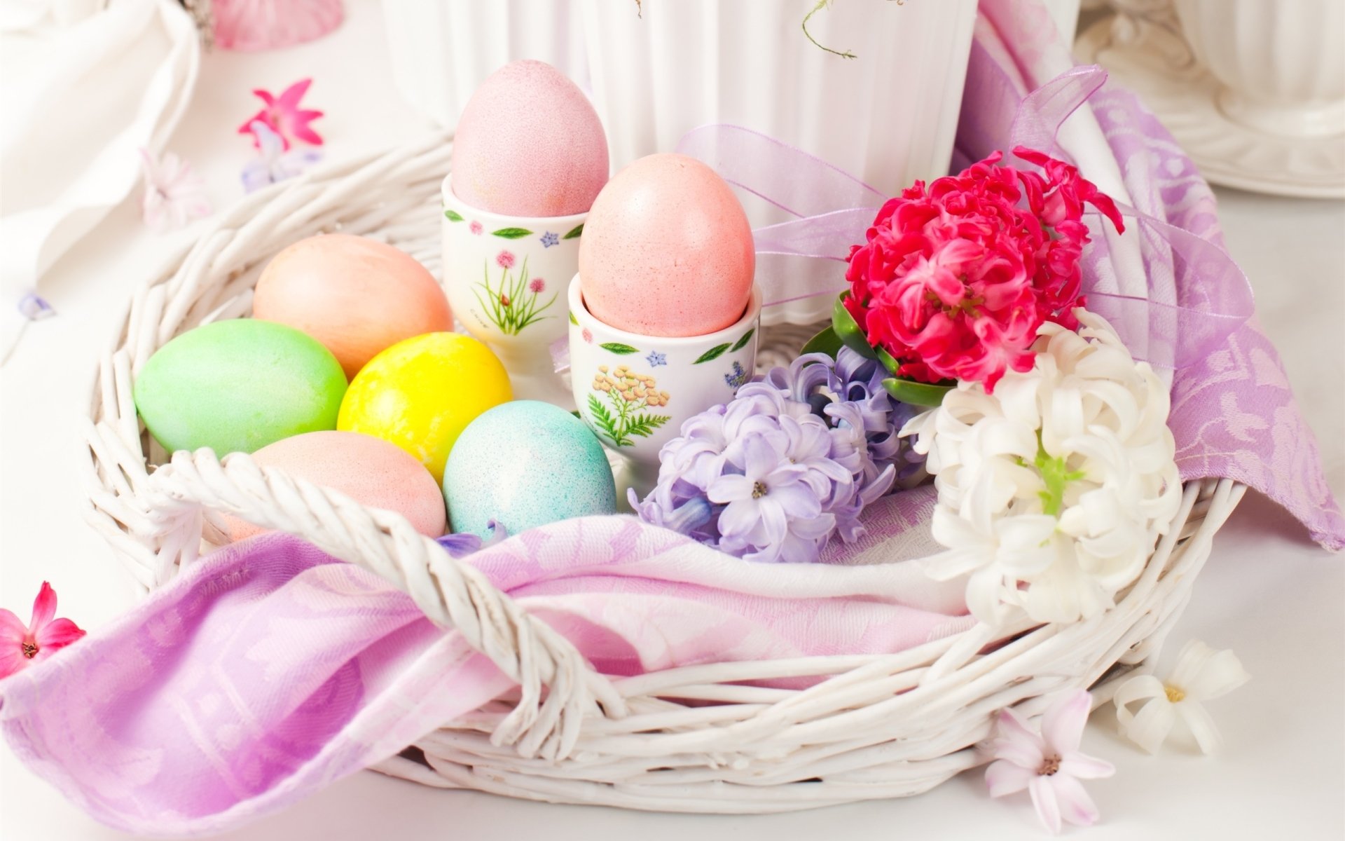 Pastel Easter still life holiday arrangement: hyacinths and blooms with colorful Easter eggs in a white woven basket — 2K Quad HD PC desktop wallpaper/background.