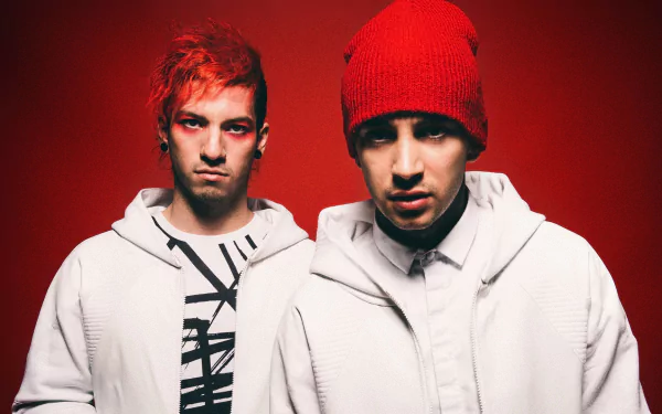 HD desktop wallpaper featuring the music duo Twenty One Pilots, posed against a bold red background. Both are wearing white outfits, with one member sporting a red beanie and the other with red-tinted hair.