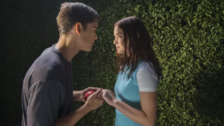 HD desktop wallpaper of two young people exchanging a red apple beside a hedge, a cinematic still evocative of the movie The Giver.