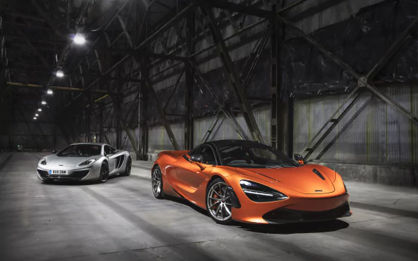 Two McLaren 720S supercars, one silver and one orange, parked inside a spacious industrial warehouse, captured in stunning 8K Ultra HD for PC desktop wallpaper.