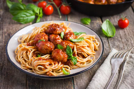 HD desktop wallpaper of a still life featuring a plate of spaghetti with meatballs, garnished with fresh basil, and surrounded by tomatoes and basil leaves.