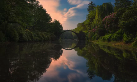 HD desktop wallpaper of Devil's Bridge reflecting over a calm river surrounded by lush nature at sunset.
