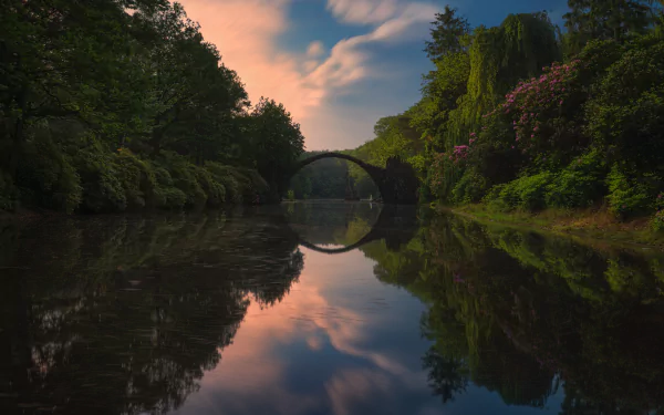 HD desktop wallpaper of Devil's Bridge reflecting over a calm river surrounded by lush nature at sunset.