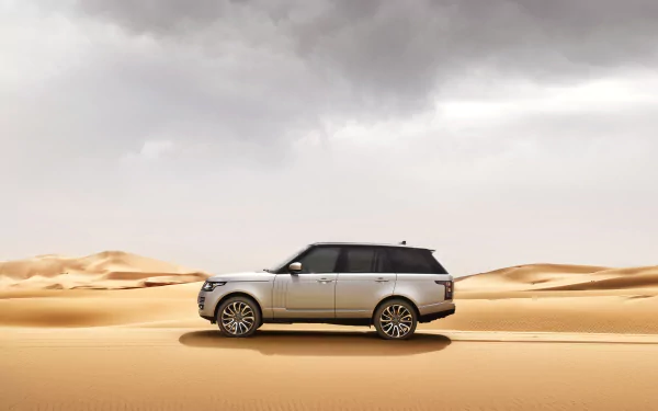 Silver Range Rover SUV drives across sandy desert under a cloudy sky in this 4K Ultra HD PC desktop wallpaper and background.