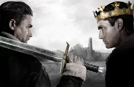 HD wallpaper of Jude Law and Charlie Hunnam in a dramatic confrontation from King Arthur: Legend of the Sword, with a sword and crown, set against a moody backdrop.