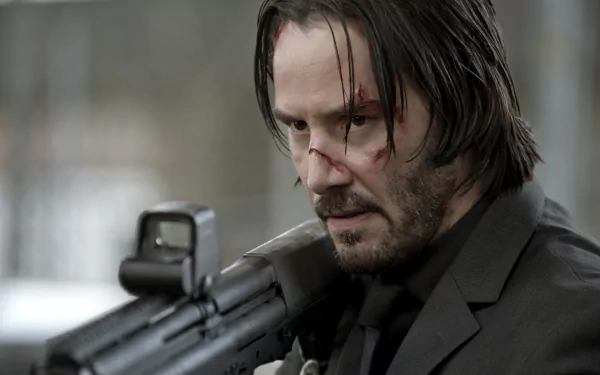 HD desktop wallpaper featuring Keanu Reeves as John Wick, with a determined expression and a slightly bloodied face, holding a gun.