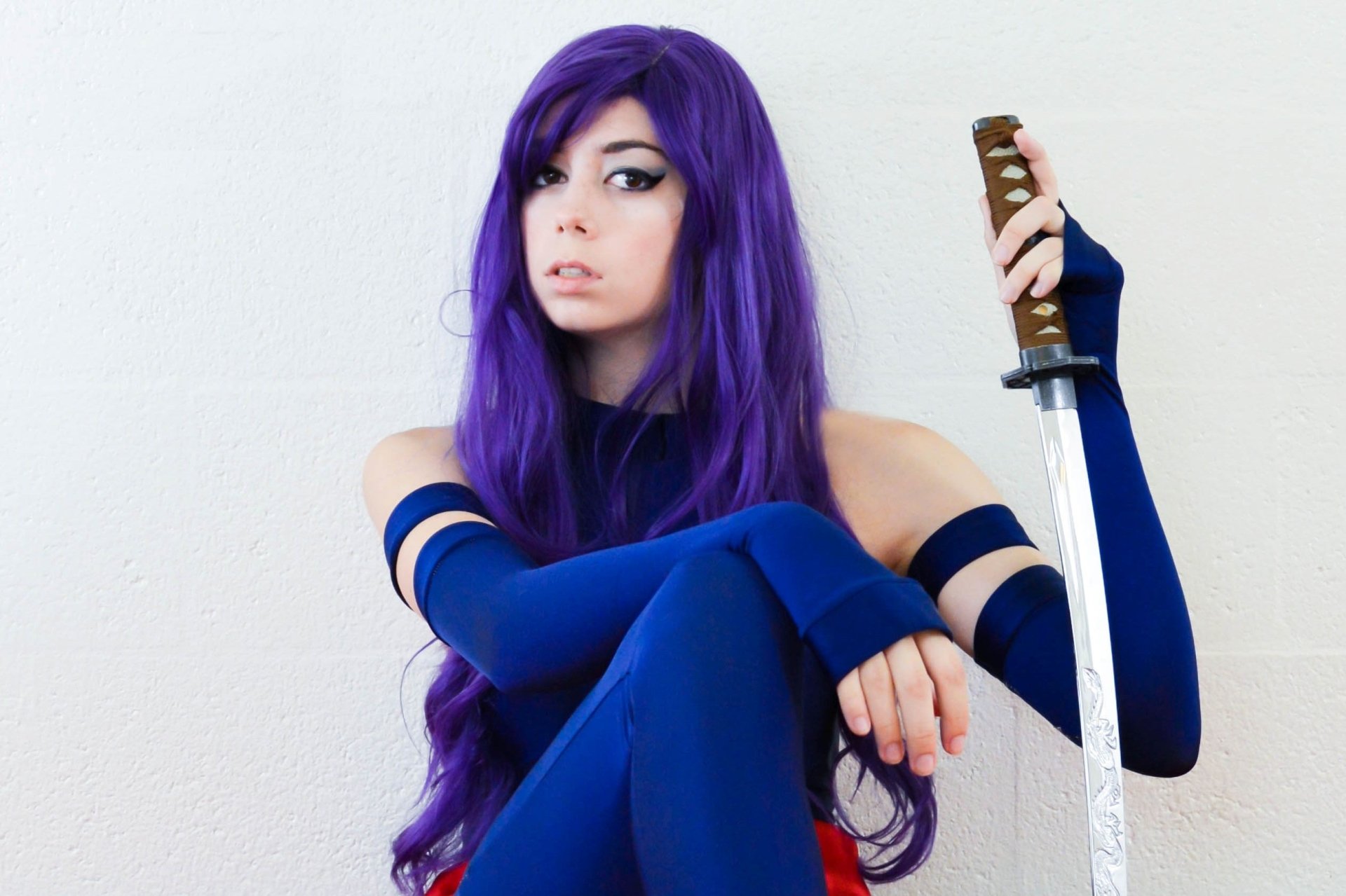 A woman cosplaying as Psylocke from Marvel Comics' X-Men, with purple hair and a blue outfit, holding a katana sword. HD desktop wallpaper and background.