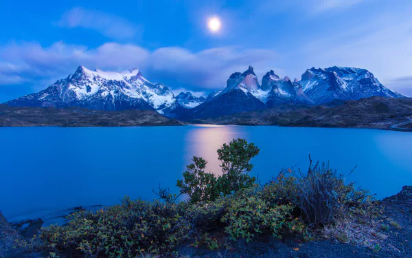 Nighttime landscape of Torres del Paine in Chile under a bright moon, with twilight hues reflecting on a calm lake, captured in 4K Ultra HD quality.