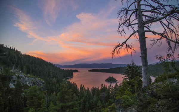 Sunset over Emerald Bay at Lake Tahoe, framed by forested mountains and calm water, captured in a vibrant HD desktop wallpaper.