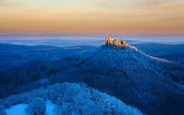 HD wallpaper featuring Hohenzollern Castle in Germany. The winter landscape showcases snow-covered hills and a stunning horizon.