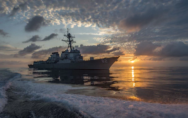 USS Lassen (DDG-82) destroyer sails on a calm ocean at sunset, with dramatic clouds and a glowing horizon in this HD military warship wallpaper.
