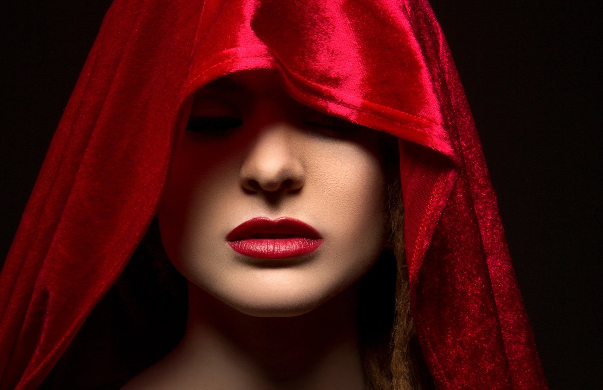 HD PC desktop wallpaper featuring a close-up of a woman’s face partially covered by a red velvet hood, with bold red lipstick highlighting her lips.