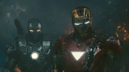 HD desktop wallpaper featuring War Machine and Iron Man from the movie Iron Man 2. Both characters stand in battle-damaged suits, glowing eyes and arc reactors, with a dark, smoky background.