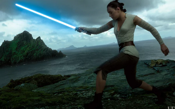 Rey from Star Wars: The Last Jedi wields a blue lightsaber on a rocky coastline under a cloudy sky. This HD desktop wallpaper features Daisy Ridley's character in an iconic pose.
