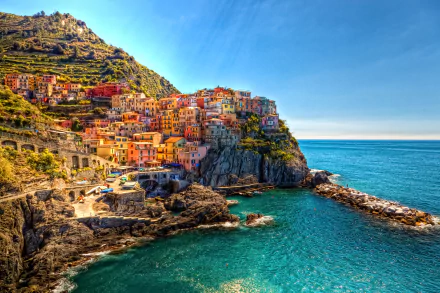 Vibrant coastal village of Cinque Terre, Liguria, Italy, with colorful houses perched on rocky cliffs overlooking the clear blue sea under a bright sky.