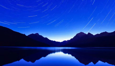 Nighttime mountain landscape with blue star trails reflected in a calm lake, creating a serene nature scene in HD quality for a PC desktop wallpaper and background.
