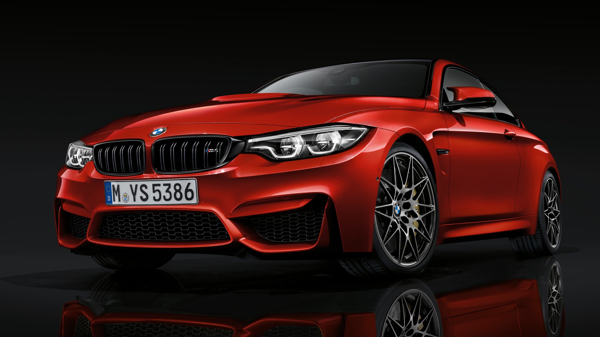 Red BMW M4 Coupe front three-quarter view with glossy reflection on black floor, high-detail 2K Quad HD PC desktop wallpaper.