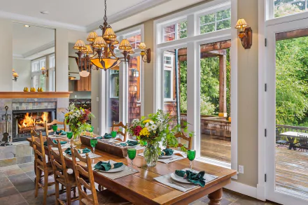 HD PC desktop wallpaper: bright man-made dining room interior with wooden table and chairs, lit fireplace, chandelier, large windows and doors opening to a green patio; decorative table settings.